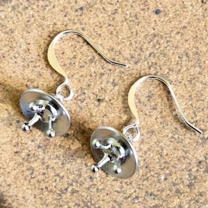 May include: A pair of silver earrings with a unique design. Each earring features a small, round disc with a raised, three-pronged design in the center.