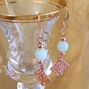 May include: Rose gold earrings with a white bead and a delicate filigree design.