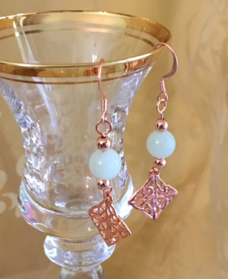 May include: Rose gold earrings with a white bead and a delicate filigree design.