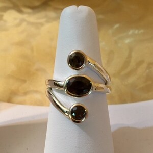 Peut inclure: Une bague en argent avec trois pierres ovales brun fonc&eacute; serties dans une bande torsad&eacute;e.