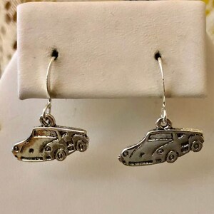 May include: A pair of silver dangle earrings featuring a detailed car design. The earrings are on a white display card.