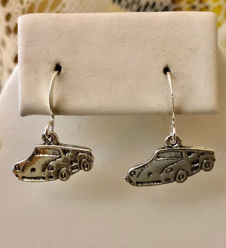 May include: A pair of silver dangle earrings featuring a detailed car design. The earrings are on a white display card.