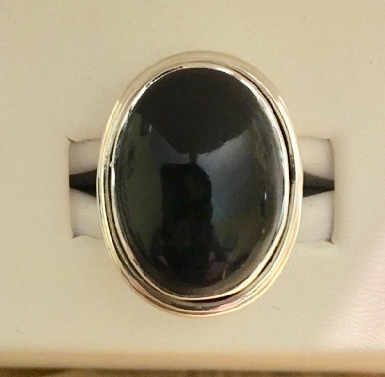 Op de afbeelding: Een zilveren ring met een grote, ovale zwarte edelsteen.