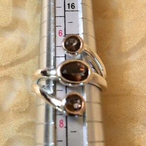 Peut inclure: Une bague en argent avec trois pierres pr&eacute;cieuses brunes. La bague est dimensionn&eacute;e sur un calibre de bague qui indique une taille 6.
