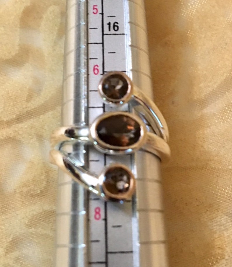 Peut inclure: Une bague en argent avec trois pierres pr&eacute;cieuses brunes. La bague est dimensionn&eacute;e sur un calibre de bague qui indique une taille 6.
