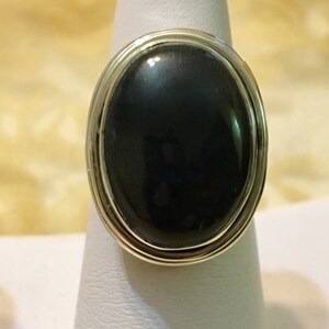 Op de afbeelding: Een zilveren ring met een grote ovale zwarte edelsteen.