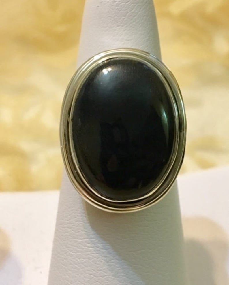 Op de afbeelding: Een zilveren ring met een grote ovale zwarte edelsteen.