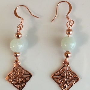 May include: A pair of copper earrings with a white stone bead and a copper filigree charm. The earrings have a hook closure.