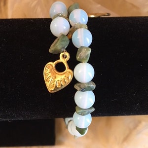 May include: A double-strand bracelet with white opal and green jasper beads. A gold heart charm hangs from the bracelet.