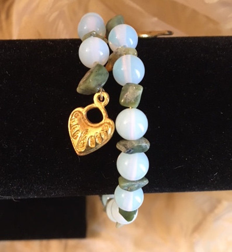 May include: A double-strand bracelet with white opal and green jasper beads. A gold heart charm hangs from the bracelet.