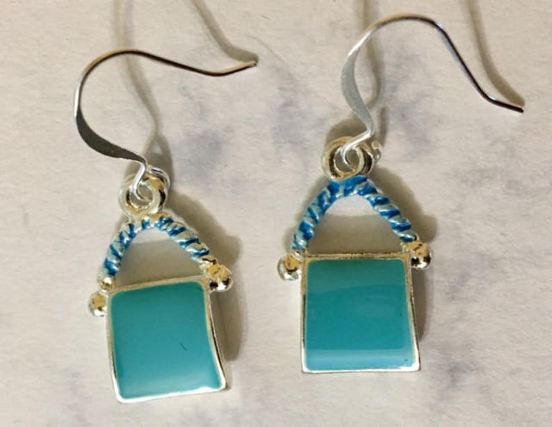 Pu&ograve; includere: Un paio di orecchini pendenti in argento con un design a corda blu e bianca e un ciondolo quadrato blu turchese.