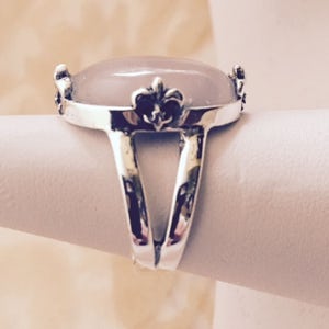 May include: A silver ring with a large oval-shaped pink stone and a fleur-de-lis design on the band.