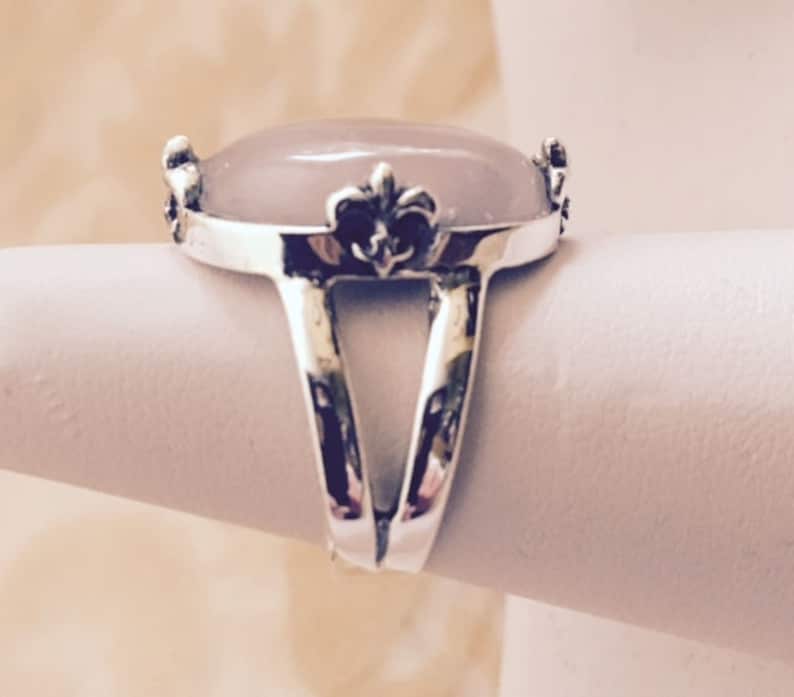 May include: A silver ring with a large oval-shaped pink stone and a fleur-de-lis design on the band.