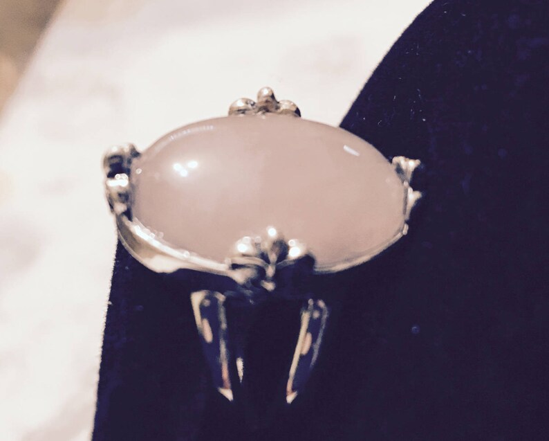 May include: A silver ring with a large, oval-shaped, pale pink gemstone set in a decorative, ornate setting.