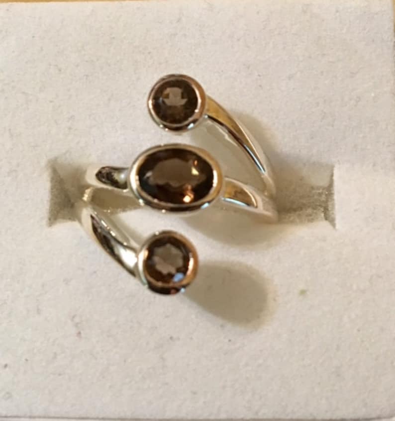 Peut inclure: Une bague en argent avec trois pierres ovales brunes. La bague est con&ccedil;ue avec une bande torsad&eacute;e.