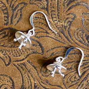 May include: A pair of silver dangle earrings with a small, round, textured design. The earrings have a simple hook closure.