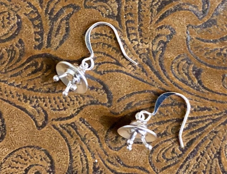 May include: A pair of silver dangle earrings with a small, round, textured design. The earrings have a simple hook closure.