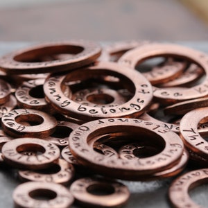 May include: A close-up of a pile of copper-colored metal rings with various engraved words and phrases, including "I am a", "Mommy belongs to", and "Never Enough".