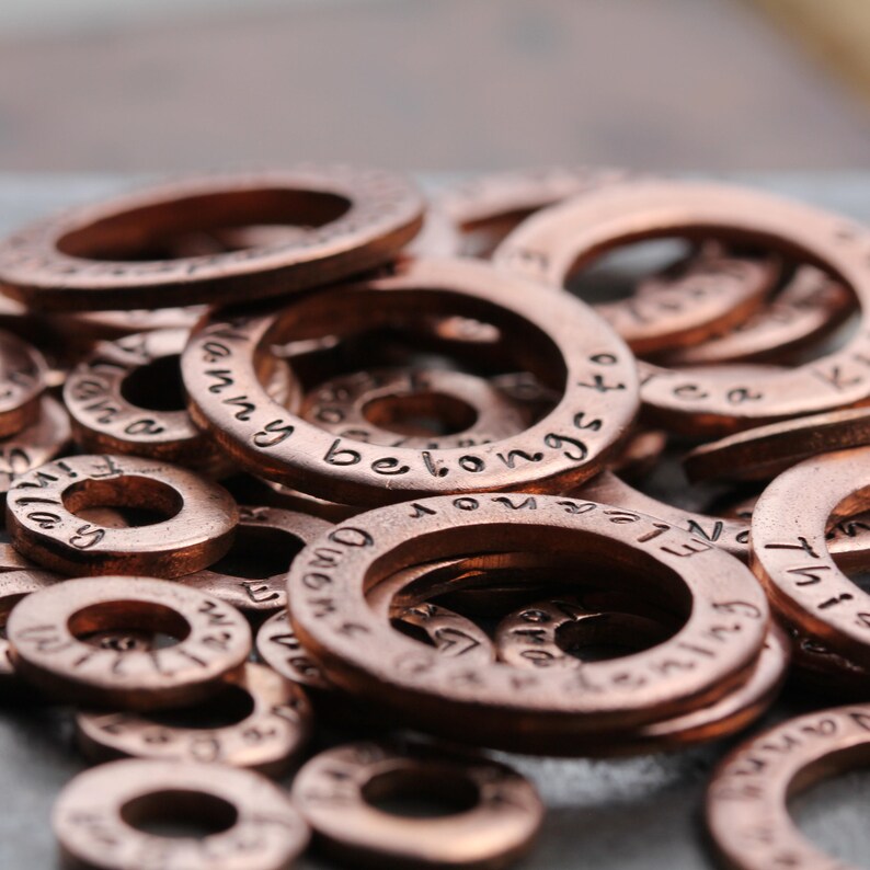 May include: A close-up of a pile of copper-colored metal rings with various engraved words and phrases, including "I am a", "Mommy belongs to", and "Never Enough".