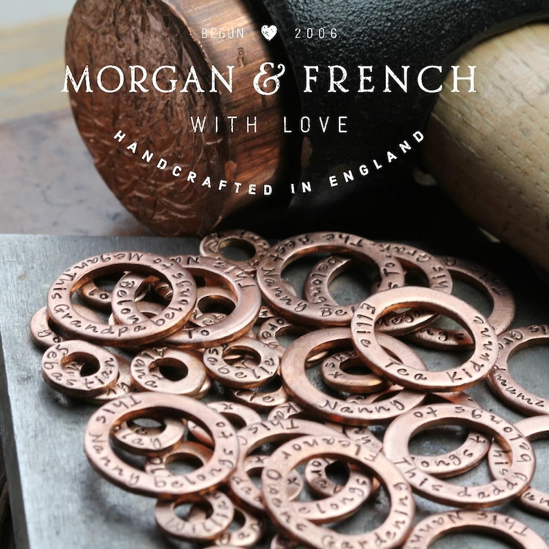May include: A close-up of a pile of copper-colored metal rings with various engraved words and phrases, including "Nanny", "Grandparents", "This is", "Tea Kid", and "Ellie".
