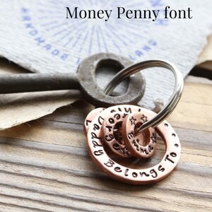 May include: A copper keychain with multiple circular charms. The charms are engraved with the words "Daddy", "Mommy", "Emma", and "Belongs To".