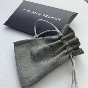 May include: A gray drawstring pouch with the text "Morgan & French" printed on it. The pouch is made of a textured fabric and has a white drawstring.