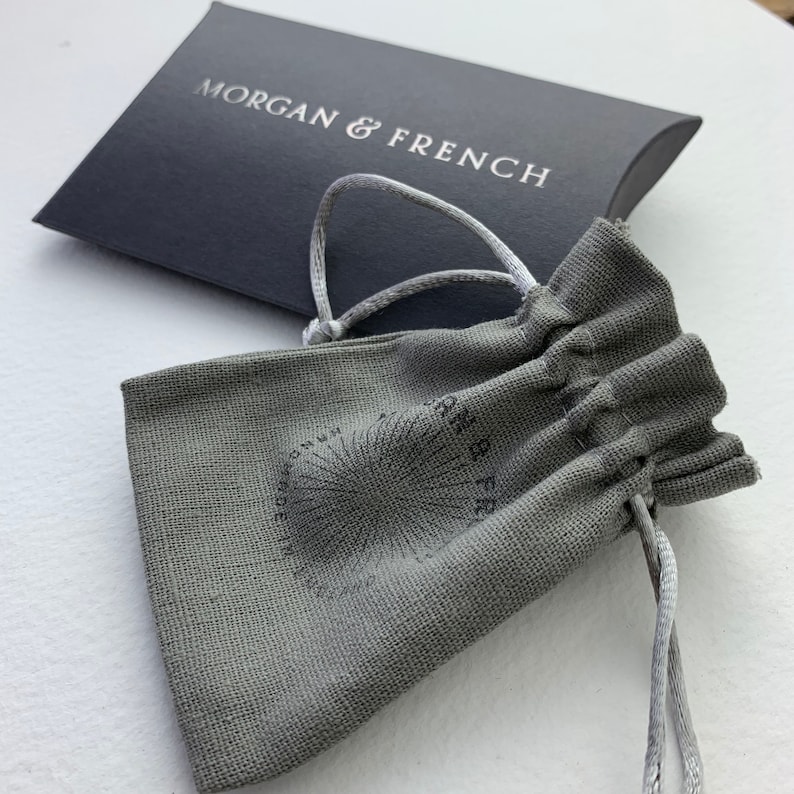 May include: A gray drawstring pouch with the text "Morgan & French" printed on it. The pouch is made of a textured fabric and has a white drawstring.