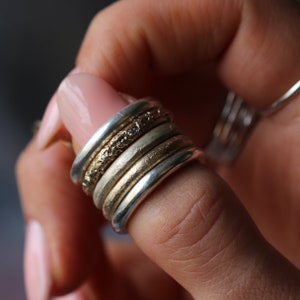Op de afbeelding: Een stapel van vijf zilveren en gouden ringen met een textuurontwerp. De ringen worden aan een vinger gedragen.