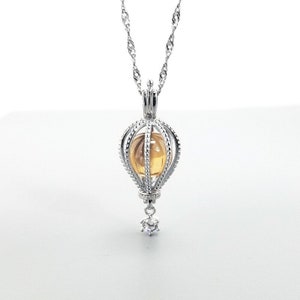 Peut inclure: Un collier en argent avec un pendentif en cage contenant une pierre précieuse jaune et un petit charme en cristal.