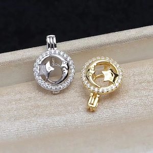 Könnte beinhalten: Zwei silberne und goldene Perlenkäfig-Anhänger mit einem Halbmond- und Sternendesign. Die Anhänger sind mit klaren Zirkonia-Steinen verziert.