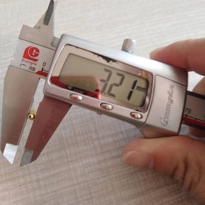 Puede incluir: Un calibre digital plateado que mide un peque&ntilde;o objeto dorado. El calibre muestra 3,21 mm.