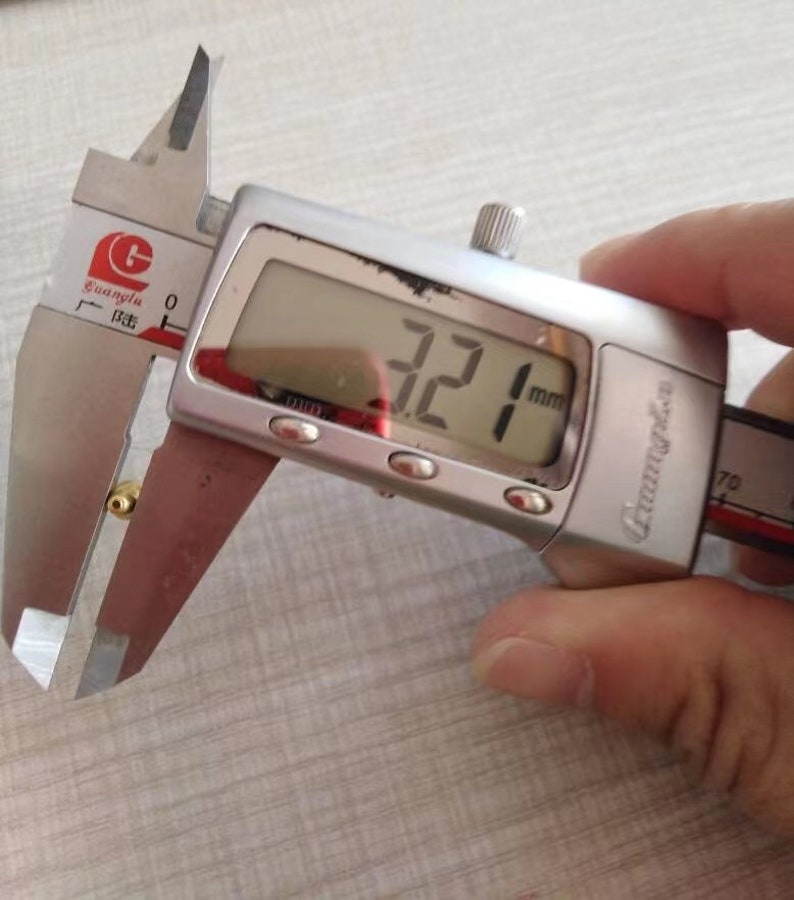 Puede incluir: Un calibre digital plateado que mide un peque&ntilde;o objeto dorado. El calibre muestra 3,21 mm.