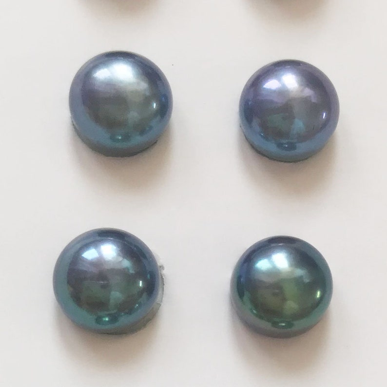May include: Four iridescent blue-green pearls on a white background. The pearls are round and smooth.