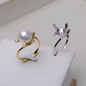 May include: Two rings with a pearl setting. The ring on the left is gold with a white pearl and small clear stones. The ring on the right is silver with a clear stone setting.