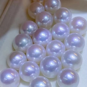 May include: A cluster of white pearls of varying sizes, arranged in a group. The pearls have a smooth, glossy finish and a subtle iridescent sheen.