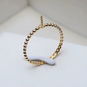 May include: A gold beaded ring with a small, vertical post extending from the top. The ring is made of small, round beads that are evenly spaced.