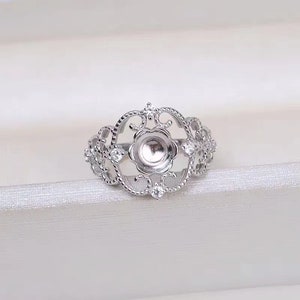 May include: Silver ring with a filigree design and a round bezel for a cabochon stone. The ring is set with small clear stones.