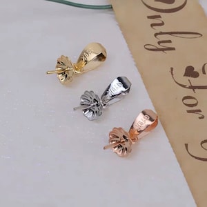 May include: Three pendant bails in gold, silver, and rose gold. Each bail has a loop at the top and a decorative flower-shaped base.