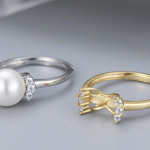 May include: Two silver rings with clear stones. One ring has a large white pearl in the center. The other ring has a delicate design with clear stones.