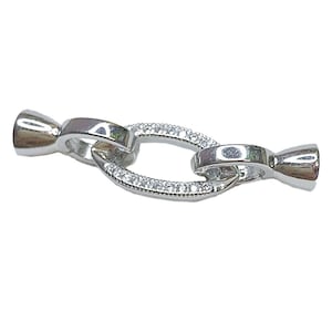 May include: Silver tone oval shaped clasp with a row of clear rhinestones around the edge.