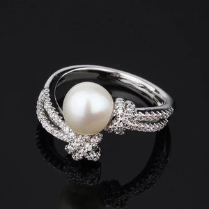 May include: A silver ring featuring a large white pearl and smaller clear stones set in a twisted band.
