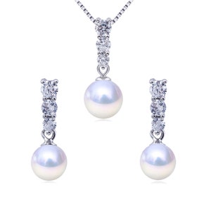 May include: A pearl and crystal necklace and earrings set. The necklace features a single pearl pendant with a row of crystals above it. The earrings are similar, with a single pearl drop and a row of crystals above it.