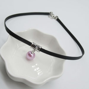May include: A black choker necklace with a silver charm and a pink pearl pendant.