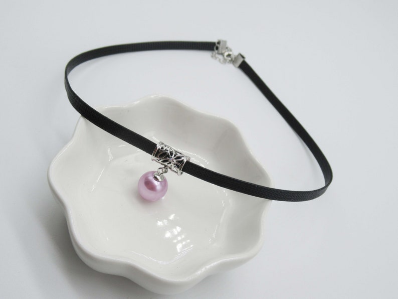 May include: A black choker necklace with a silver charm and a pink pearl pendant.