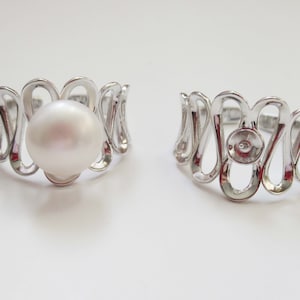 May include: Two silver rings with a wavy design. One ring has a white pearl set in the center.