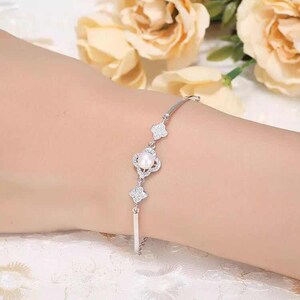 May include: A silver bracelet with a delicate chain and three clover-shaped charms. Each charm is adorned with sparkling cubic zirconia stones and a single pearl in the center.
