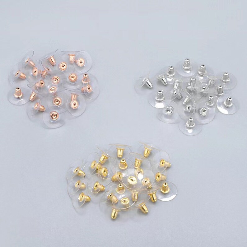 Puede incluir: Tres pilas de respaldos de pendientes, cada uno con un color de metal diferente: oro, plata y oro rosa. Los respaldos son de pl&aacute;stico transparente con un poste de metal.