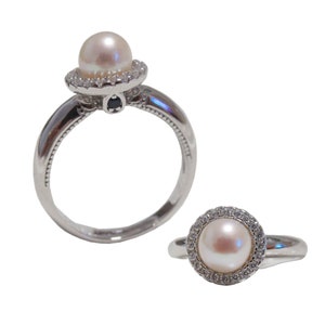 Könnte beinhalten: Silberner Ring mit einer hellrosa Perle, umgeben von kleinen, klaren Edelsteinen. Ein kleiner schwarzer Edelstein akzentuiert das Design des Rings. Ein zweiter Ring mit ähnlichem Design ist ebenfalls abgebildet.