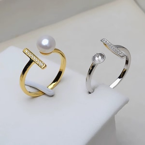 May include: Two rings with a bar design. The ring on the left is gold with a pearl and clear stones. The ring on the right is silver with clear stones.