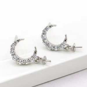 May include: A pair of silver crescent moon earring findings with clear crystal accents. The findings have a post and butterfly backing.
